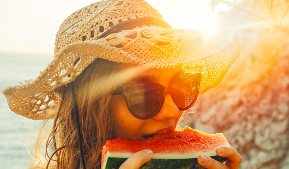 BBGR, femme avec un chapeau, portant des lunettes équipées de verres solaire et mangeant une part de pastèque, en été.